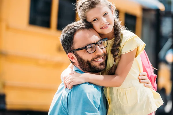 Padre abbracciando la sua figlioletta davanti allo scuolabus — Foto stock