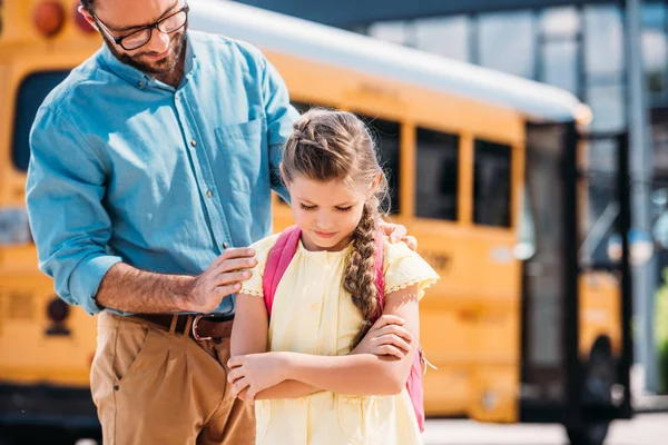 Father supporting his depressed daughter in front of school bus — Stock Photo