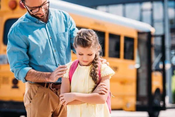 Padre apoyando a su hija deprimida frente al autobús escolar - foto de stock