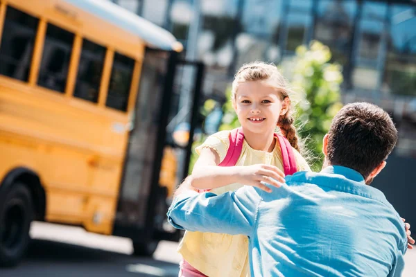 Вид сзади отца и дочери, сидящих перед школьным автобусом — стоковое фото