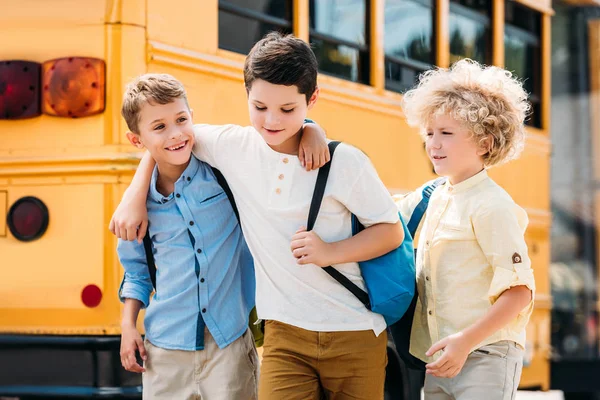 Fröhliche kleine Schulbuben, die gemeinsam vor dem Schulbus Spaß haben — Stockfoto