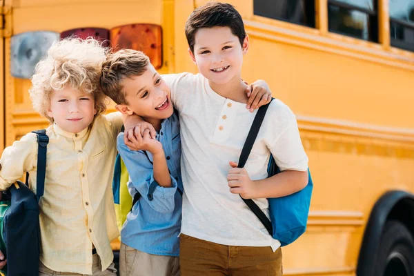 Happy little schoolboys embracing in front of school bus — Stock Photo