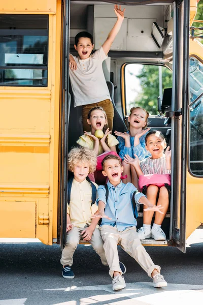 Grupo de escolares adorables sentados en las escaleras del autobús escolar y gritando - foto de stock
