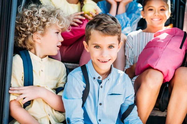 Gruppe glücklicher Schüler sitzt auf der Treppe des Schulbusses und blickt in die Kamera — Stockfoto