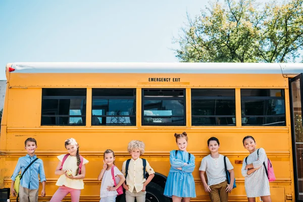 Группа очаровательных учеников, позирующих перед школьным автобусом — стоковое фото