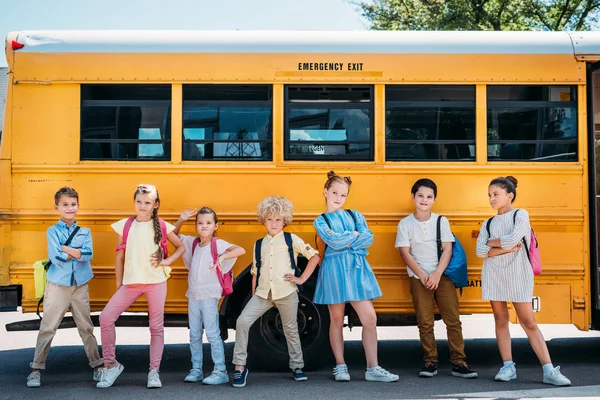 Grupo de adoráveis crianças em idade escolar posando em frente ao ônibus escolar — Fotografia de Stock