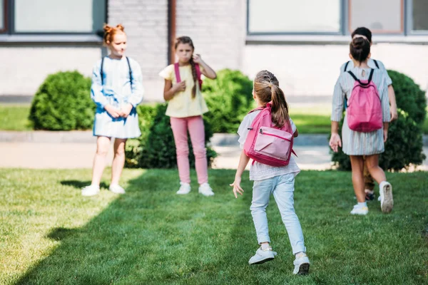 Rear view of pupils with bakpacks waling by school garden — Stock Photo
