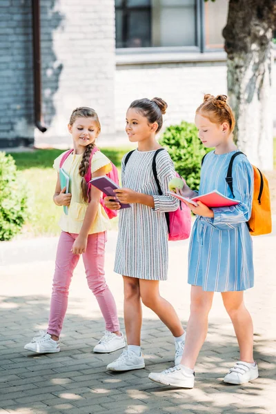 Groupe de belles écolières avec des cahiers marchant ensemble après l'école — Photo de stock