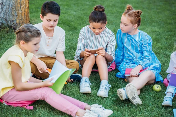 Group of adorable pupils spending time together on grass after school — Stock Photo