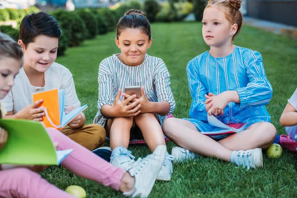 Grupo de escolares adorables pasar tiempo juntos en la hierba después de la escuela - foto de stock