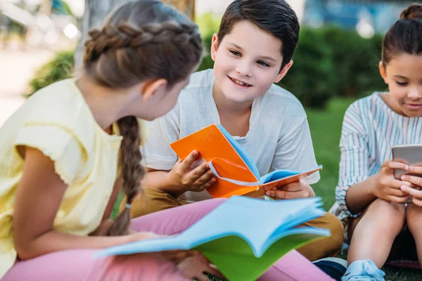 Group of adorable pupils spending time together on grass after school — Stock Photo