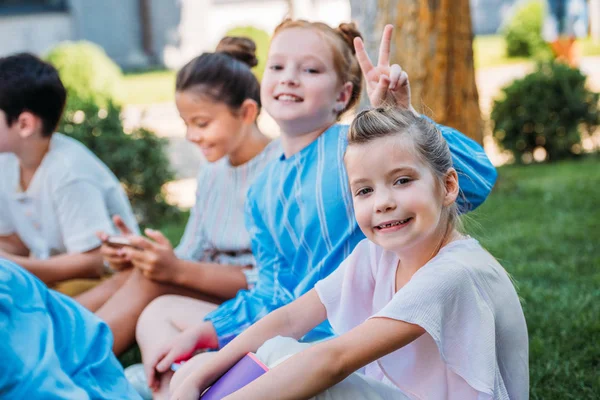 Gruppe entzückender Schulmädchen, die auf Gras sitzen und in die Kamera schauen — Stockfoto