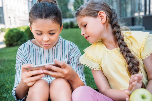 Adorable little schoolgirls using smartphone together — Stock Photo