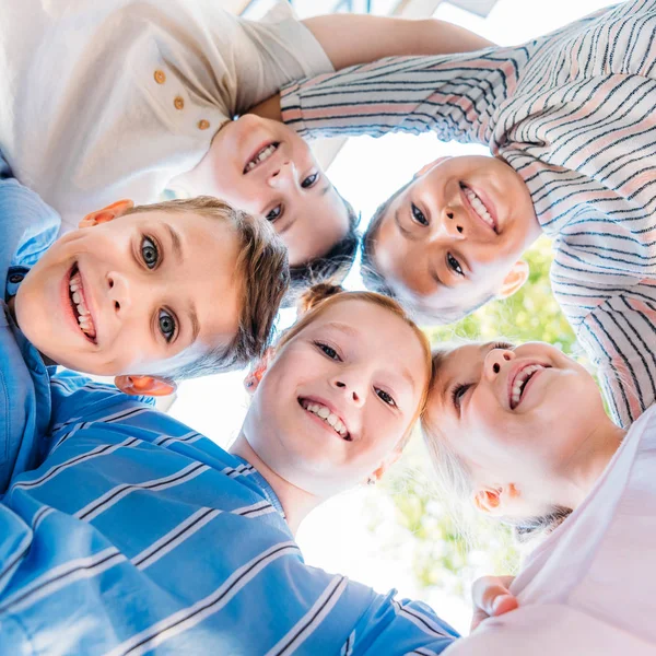 Biew inferior de grupo de escolares bonitos de pé em círculo e olhando para a câmera — Fotografia de Stock