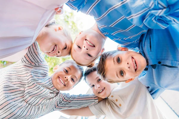 Biew bas de groupe d'écoliers souriants debout en cercle et regardant la caméra — Photo de stock