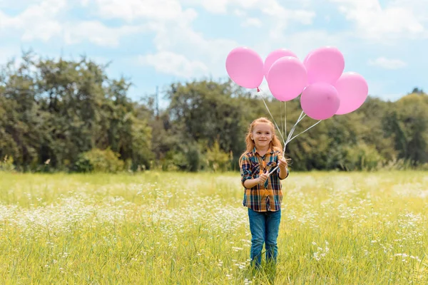 Bambino sorridente con palloncini rosa in piedi nel campo estivo — Foto stock