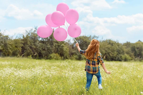 Visão traseira da criança com balões rosa em pé no campo de verão com céu azul no fundo — Fotografia de Stock