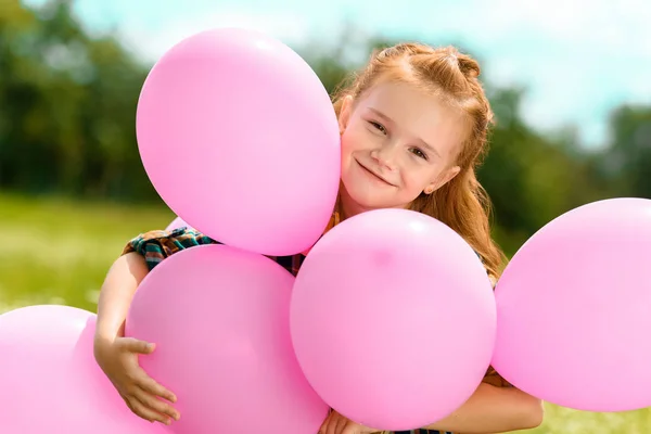 Retrato de niño lindo sonriente abrazando globos de color rosa en el campo de verano - foto de stock