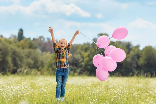 Niño feliz con globos rosados en el campo de verano - foto de stock