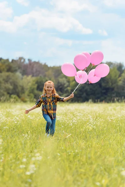 Cheerful kid with pink balloons in hand running in meadow — Stock Photo