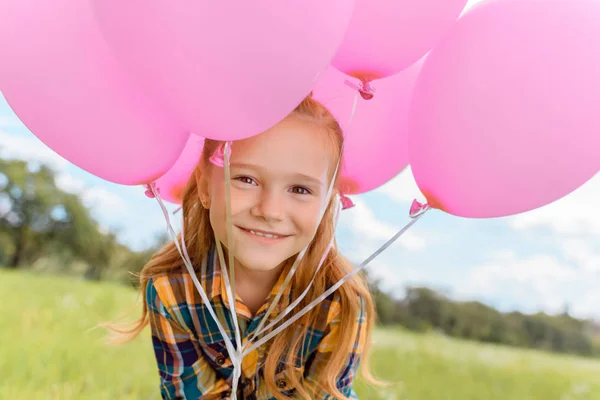 Retrato de niño lindo con globos de color rosa mirando a la cámara en el campo de verano - foto de stock