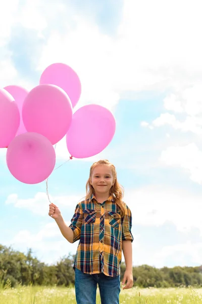 Portrait of cute child with pink balloons in summer field with blue cloudy sky on background — Stock Photo