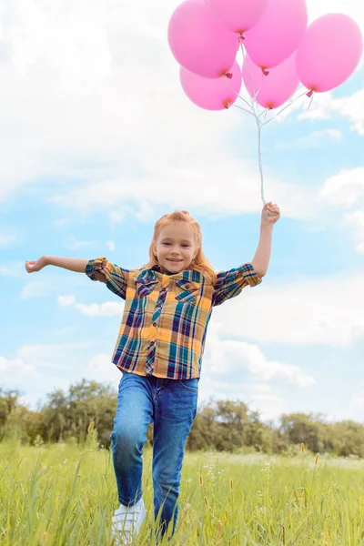 Niño alegre con globos rosados en la mano corriendo en el prado — Stock Photo