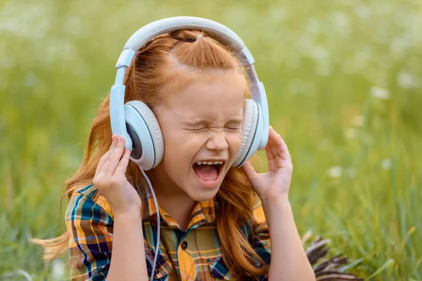 Retrato de niño gritando mientras escucha música en auriculares con hierba verde en el fondo — Stock Photo