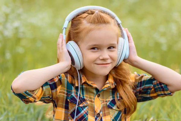 Portrait d'un enfant souriant écoutant de la musique dans un casque avec de l'herbe verte en arrière-plan — Photo de stock