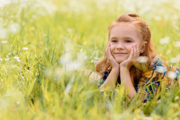 Porträt eines kleinen lächelnden Kindes, das auf grünem Gras auf einer Wiese ruht — Stockfoto