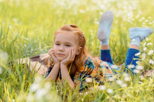 Porträt eines kleinen nachdenklichen Kindes, das auf einer Wiese auf grünem Gras ruht — Stockfoto