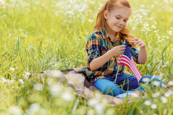 Niedliches Kind mit amerikanischer Fahnenstange ruht auf grünem Gras im Feld — Stockfoto