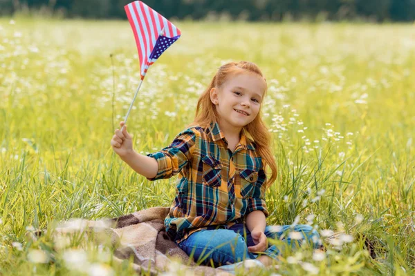 Cute kid with american flagpole resting on green grass in field — Stock Photo
