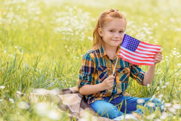 Cute kid with american flagpole resting on green grass in field — Stock Photo