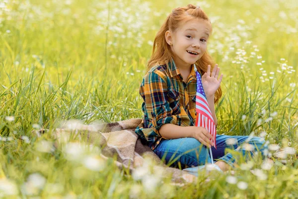Emotional kid with american flagpole resting on green grass in field — Stock Photo