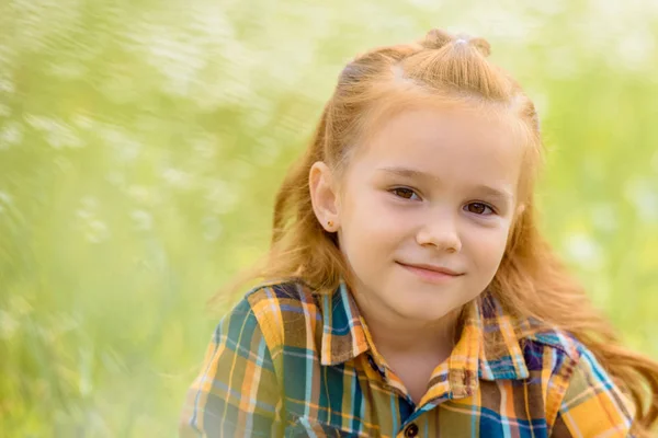 Portrait of adorable kid looking at camera with blurred green grass on background — Stock Photo
