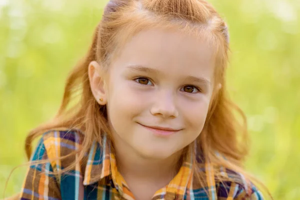 Портрет очаровательного ребенка, смотрящего в камеру с размытой зеленой травой на заднем плане — стоковое фото