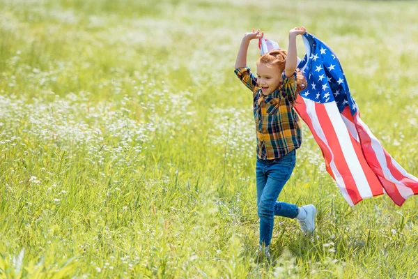 Criança feliz correndo em campo com bandeira americana em mãos — Fotografia de Stock