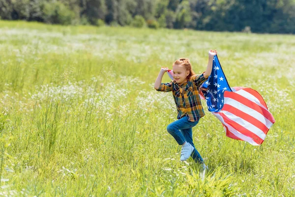 Niño corriendo en el campo con bandera americana en las manos - foto de stock