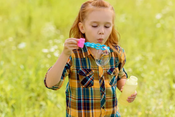 Porträt eines Kindes, das Seifenblasen auf der Wiese pustet — Stockfoto