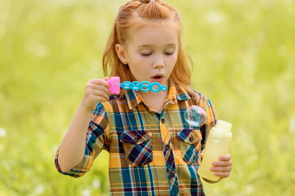Портрет ребенка, дующего мыльные пузыри на лугу — стоковое фото