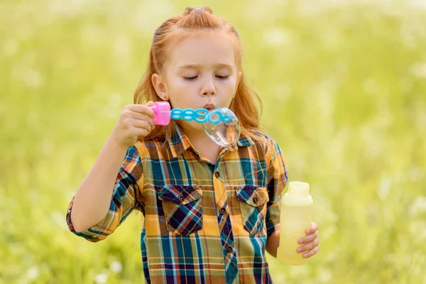 Portrait of kid blowing soap bubbles in meadow — Stock Photo