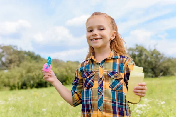 Portrait of smiling kid with soap bubbles in meadow — Stock Photo