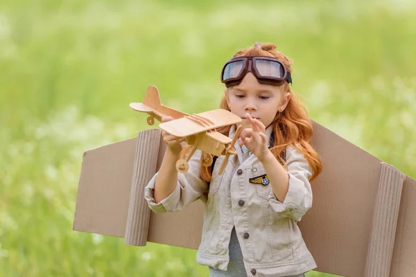 Portrait of little child in pilot costume with wooden toy plane standing in meadow — Stock Photo
