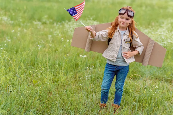 Kid in pilot costume with american flagpole standing in meadow — Stock Photo