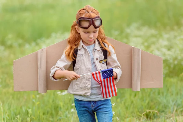 Portrait of kid in pilot costume with american flagpole standing in meadow — Stock Photo