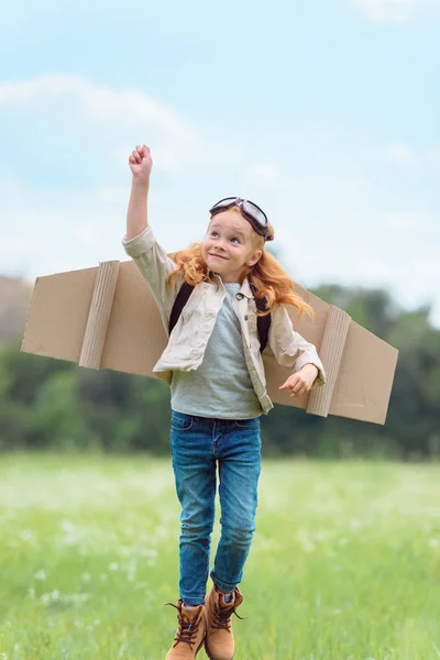 Kid in pilot costume with outstretched arm jumping in meadow — Stock Photo