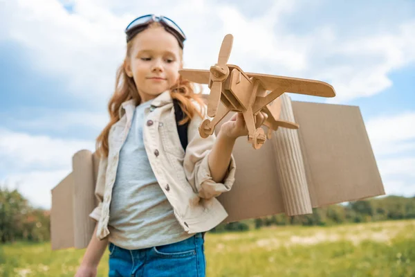 Red hair kid in pilot costume holding wooden plane in summer field — Stock Photo
