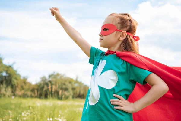 Adorable child in superhero costume with outstretched arm in summer field — Stock Photo