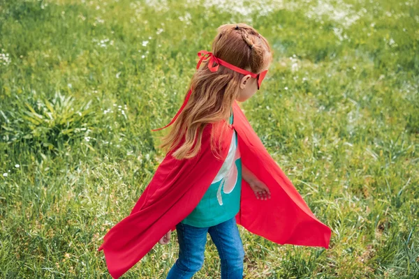 Niño pequeño en traje de superhéroe rojo de pie en el campo de verano - foto de stock